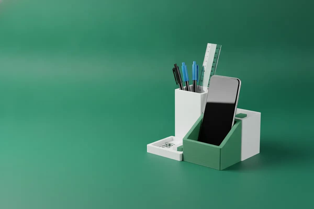 Organizador de secretária branco e verde impresso em 3D, com canetas, régua e telemóvel, sobre fundo verde.