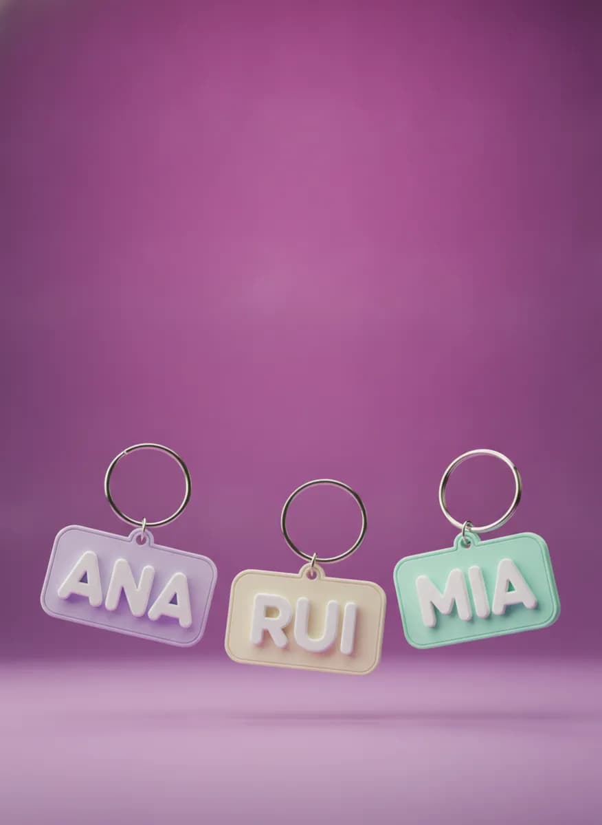 Três porta-chaves impressos em 3D com os nomes Ana, Rui e Mia, em lilás, creme e verde-menta, sobre fundo roxo.